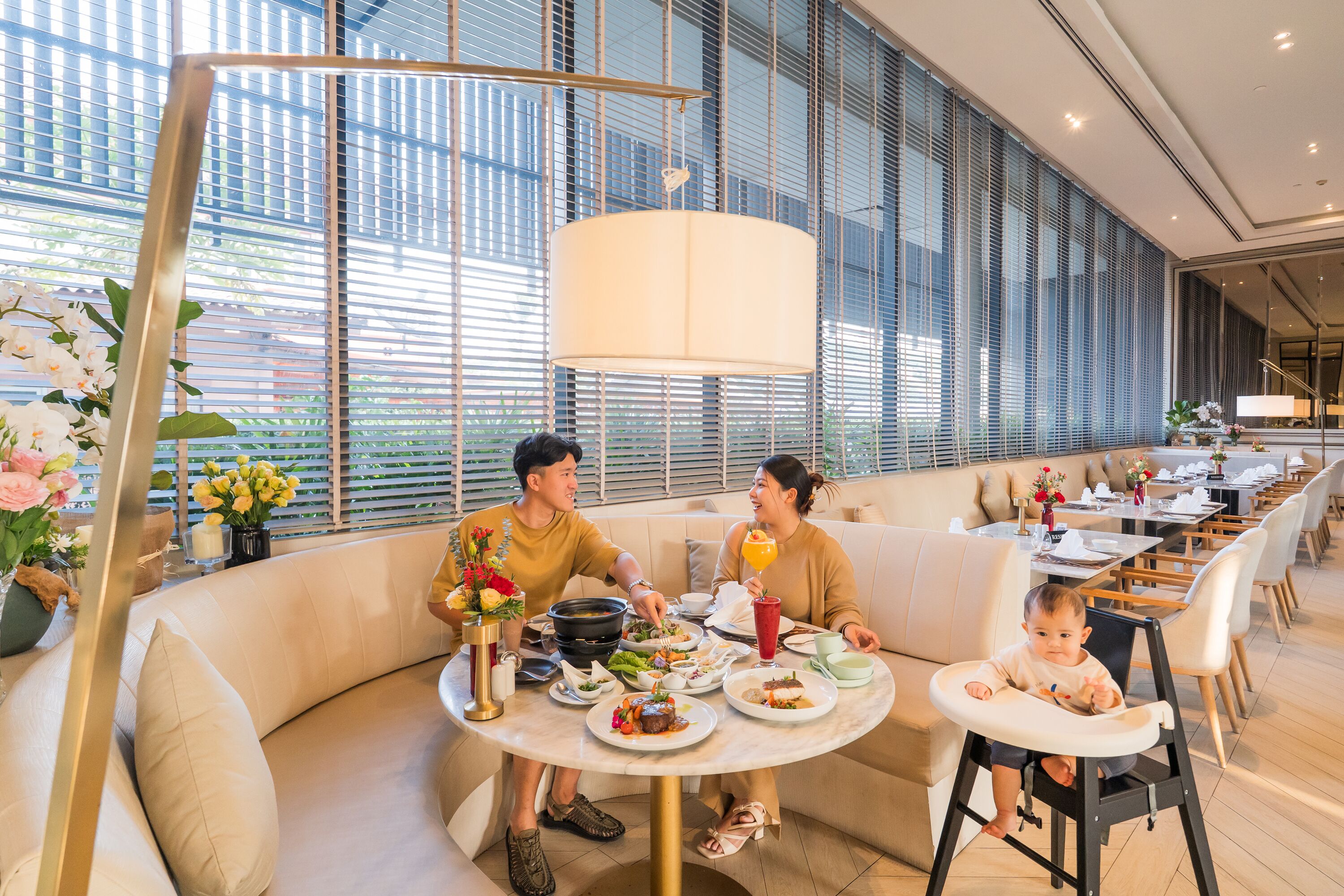 Un comedor moderno con una mesa redonda, asientos acolchados y un techo alto con grandes ventanas.