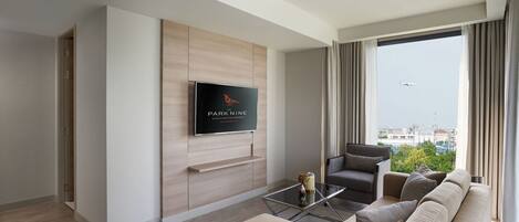 Una habitación de hotel moderna con un gran ventanal, un televisor de pantalla plana montado en la pared, un sofá, una mesita de centro y vistas de la ciudad.