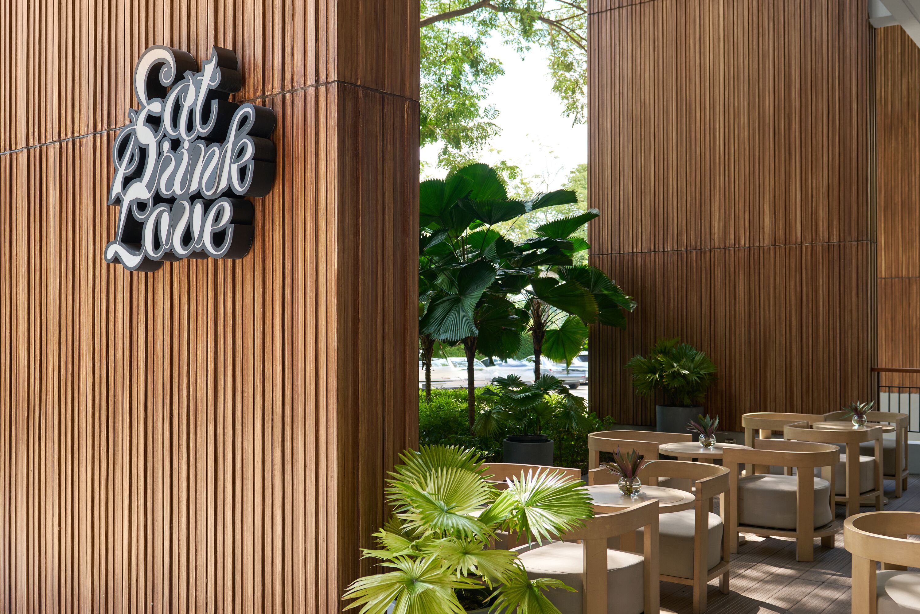 An outdoor seating area with wooden tables and chairs, surrounded by vertical wooden panels and potted plants.
