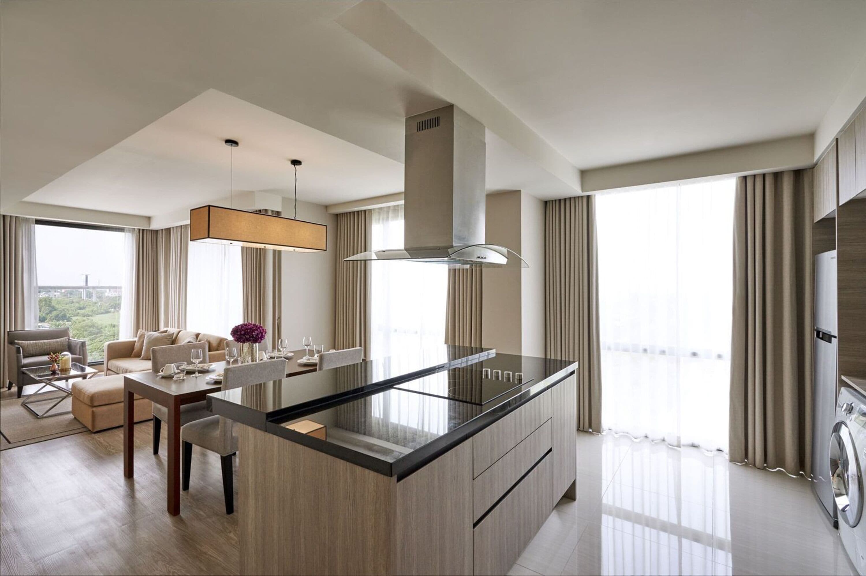 A modern kitchen with a central island, a dining area with a table and chairs, and a large window with curtains.