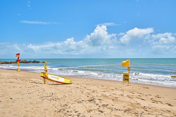A beach with lifeguard flags, a yellow lifeguard stand, and a warning sign.