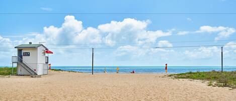 Una playa con una torre de salvavidas, cielo despejado y mar tranquilo.
