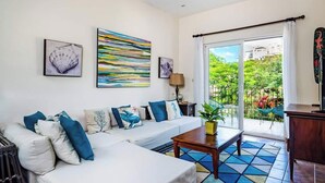 A living room with a white sofa, colorful cushions, a wooden coffee table, and a view of greenery through a sliding glass door. - La Cometa 19♆ Private rooftop terrace convenient in ♥ of town (Tamarindo)