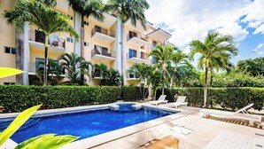 A swimming pool surrounded by palm trees and a multi-story building with balconies. - La Cometa 19♆ Private rooftop terrace convenient in ♥ of town (Tamarindo)