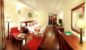 Habitación de hotel con cama, escritorio, silla, mesa con juego de té, espejo y televisión.