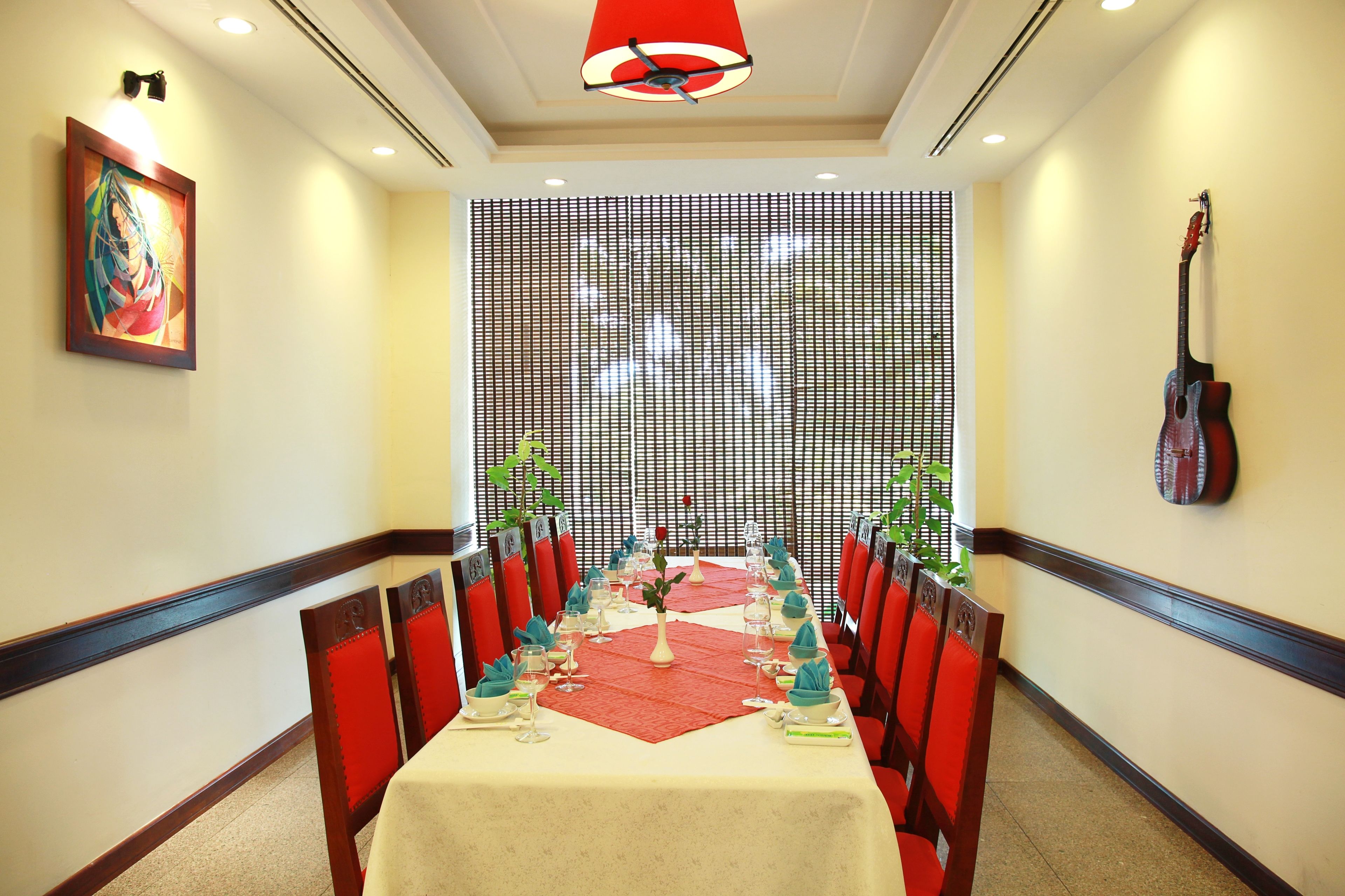 A dining area with a long table set for a meal, red chairs, a decorative wall, and a guitar on the wall.