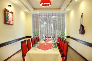 Un comedor con una mesa larga dispuesta para una comida, sillas rojas, un muro decorativo y una guitarra colgada en la pared.