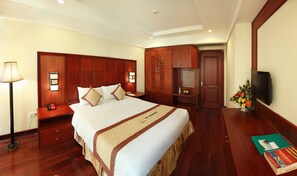 Una habitación de hotel con una cama grande, armario de madera, mesita de noche, lámpara y televisión.