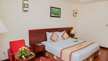 A hotel room with a wooden bed, a red chair, a small table with a flower arrangement, and a nightstand with a lamp.