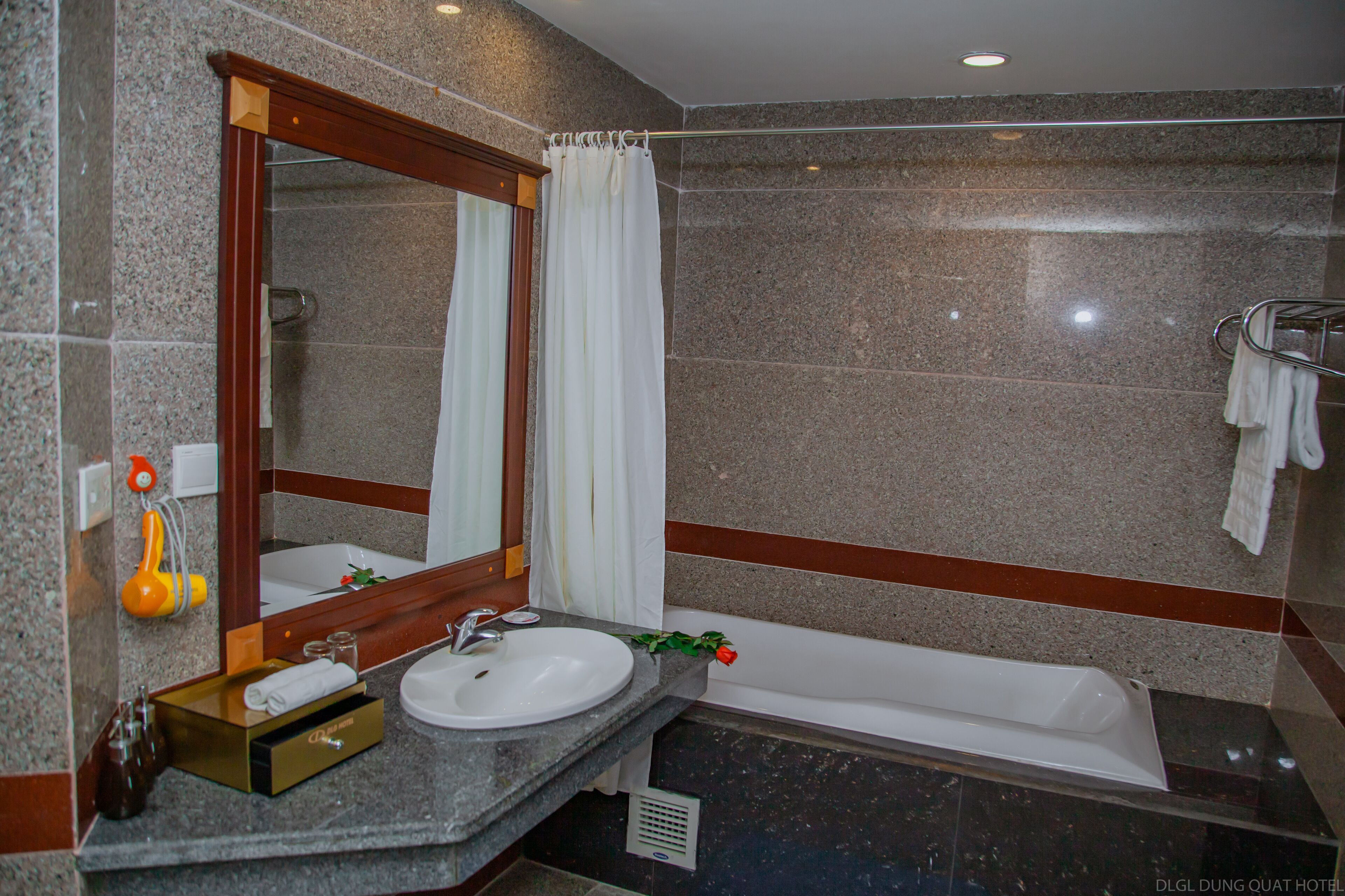 A modern bathroom with a granite countertop, a white sink, a large mirror, and a bathtub.