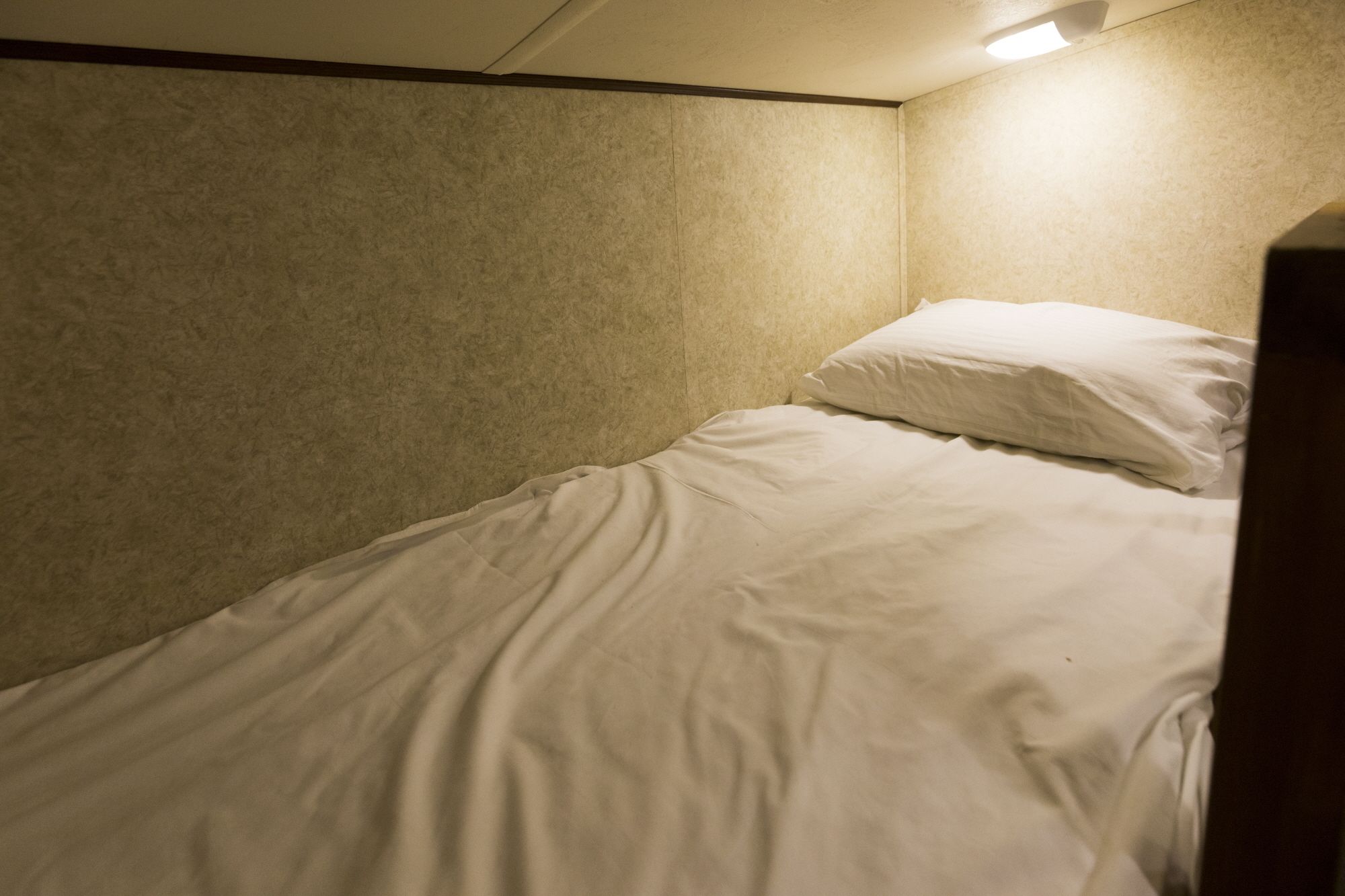 A small, single-bed room with a plain, textured wall and a ceiling light.