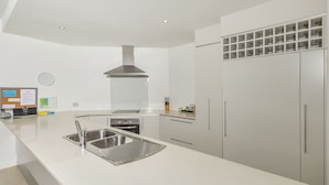 A modern kitchen with a stainless steel sink, a built-in oven, and a large refrigerator. - Peponi 4 - Beachfront Apartment (Yorkeys Knob)