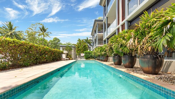 A swimming pool with clear blue water, surrounded by potted plants and a building with balconies. - Peponi 4 - Beachfront Apartment (Yorkeys Knob)