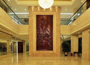 Eine geräumige Lobby mit einer großen Holzskulptur, poliertem Marmorboden und einem modernen Kronleuchter.