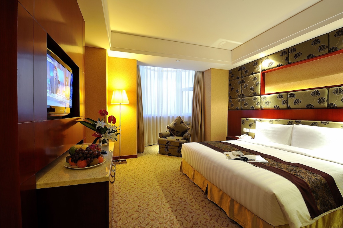 Ein Hotelzimmer mit einem Bett, einem Schreibtisch mit Fernseher, einer Lampe und einer Obstschale.