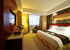 Ein Hotelzimmer mit einem Bett, einem Schreibtisch mit Fernseher, einer Lampe und einer Obstschale.