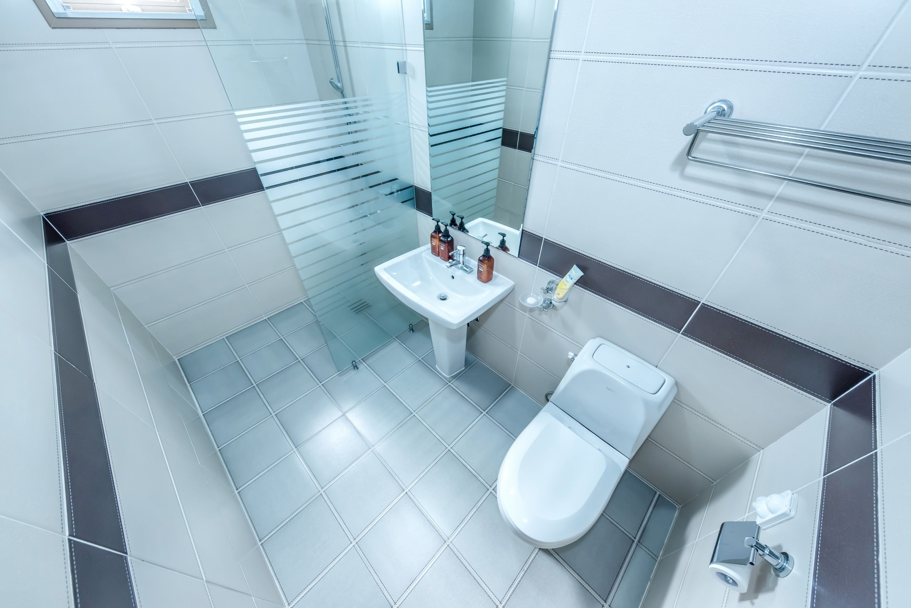 A modern bathroom with a glass shower enclosure, a white sink with soap dispensers, and a toilet.