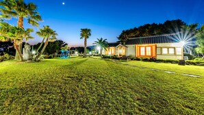 A well-lit residential area with a house, palm trees, and a clear night sky. - Stone Statue Village Hanok (Seogwipo)
