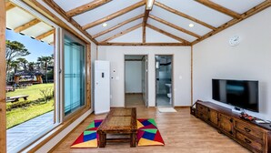 A spacious living room with a large window, wooden ceiling beams, a television, and a dining area. - Stone Statue Village Hanok (Seogwipo)