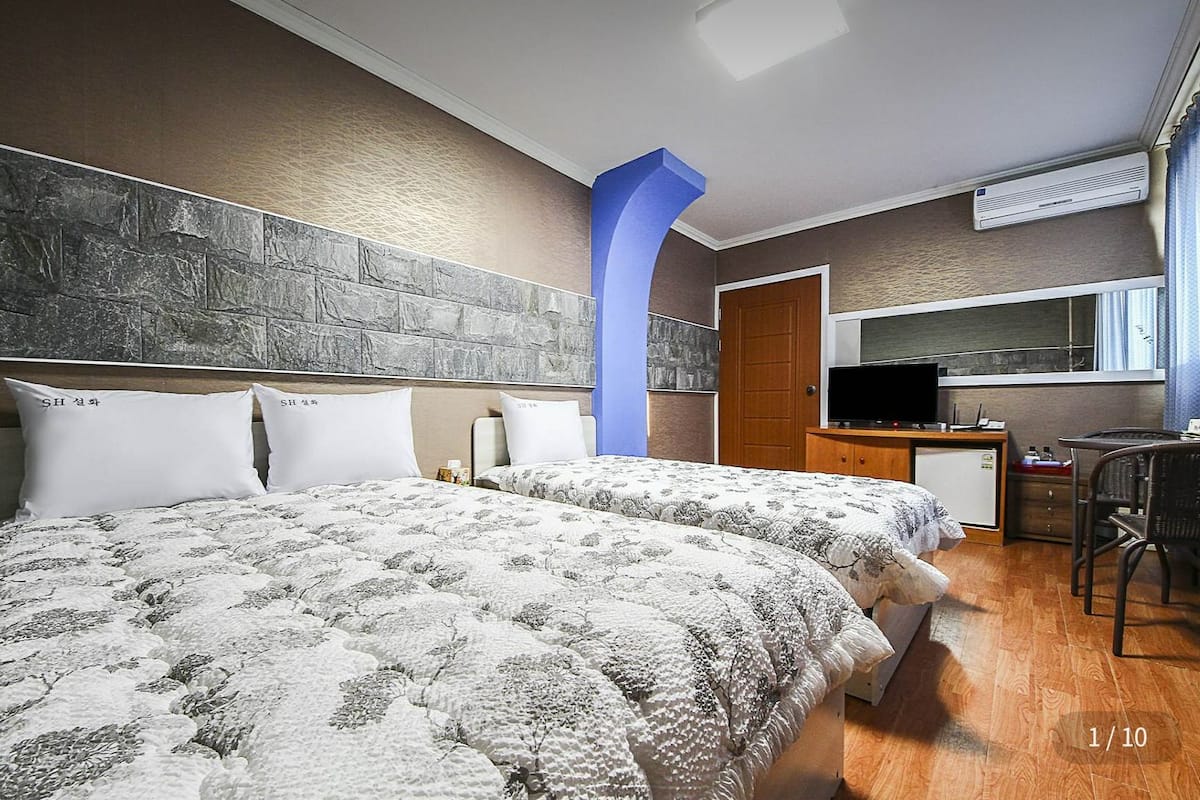 Ein Hotelzimmer mit zwei Betten, einem Schreibtisch, einem Computer, einem Fernseher und einem Fenster mit Vorhängen.
