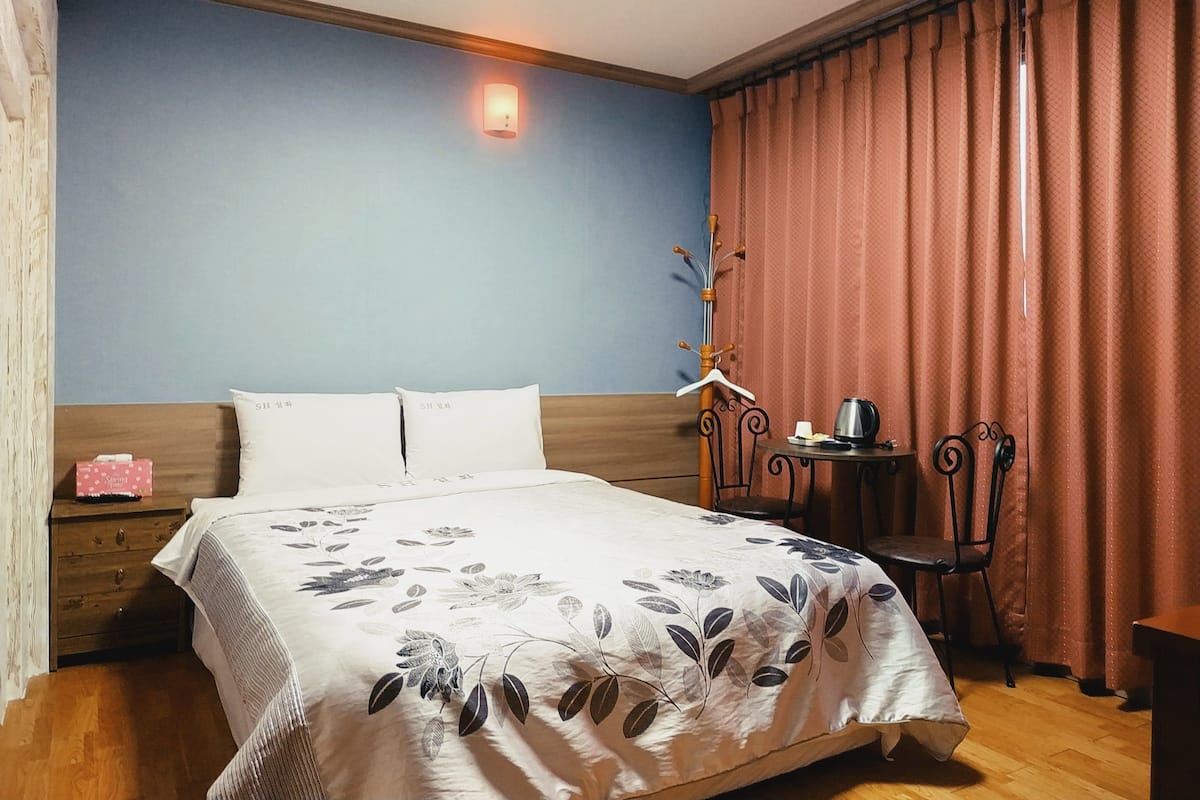 Ein Schlafzimmer mit einem Bett, einem Nachttisch, einem kleinen Tisch mit Wasserkocher und einem Sessel.