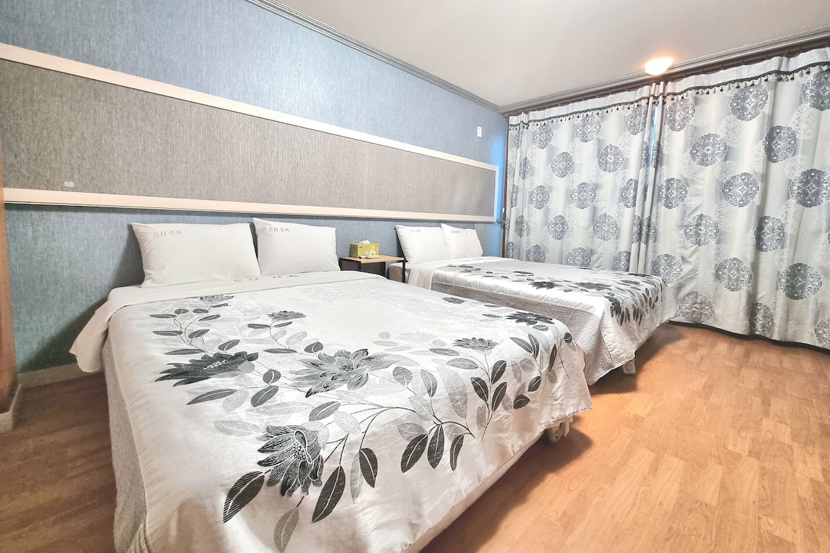 Ein Hotelzimmer mit zwei Betten, Holzboden und einem gemusterten Vorhang.