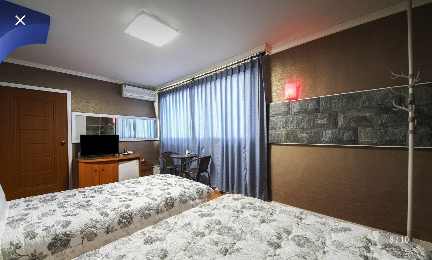 Habitación de hotel con dos camas, un escritorio con computadora, una silla, una mesita, un espejo y un adorno de pared de piedra.