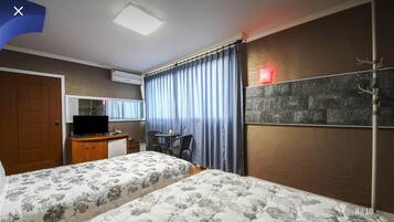 Habitación de hotel con dos camas, un escritorio con computadora, una silla, una mesita, un espejo y un adorno de pared de piedra.