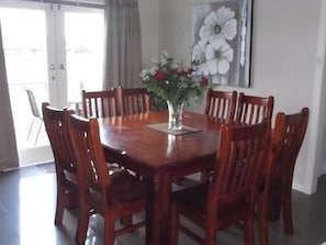 A dining area with a wooden table and chairs, a vase with flowers, and a large flower painting on the wall. - Avenue House (Moonah)