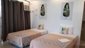 A hotel room with two beds, each with patterned bedspreads, a large window with curtains, and wall-mounted air conditioning units. - V Resort Dasma (Dasmarinas)