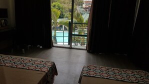 A hotel room with two beds, a view of a pool and palm trees, and a balcony with a green roof. - V Resort Dasma (Dasmarinas)
