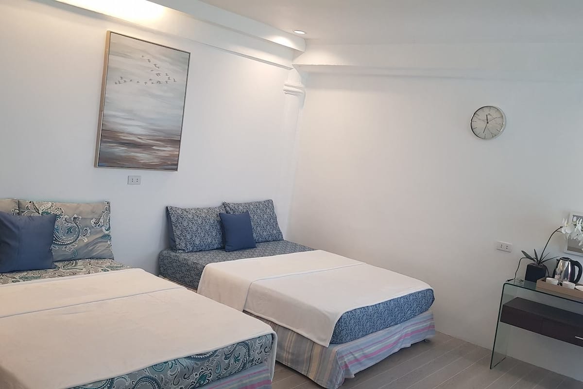 A bedroom with two beds, a bedside table, a clock, and a painting on the wall.