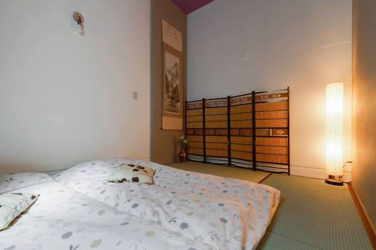 Ett rum med en säng, en futon, en traditionell japansk skjutdörr och en vägglampa.