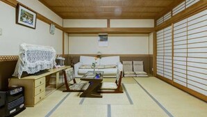 A traditional Japanese-style room with tatami flooring, a low wooden ceiling, a sofa, a coffee table, and a television on a cabinet. - Nakayama Guesthouse (Osaka)