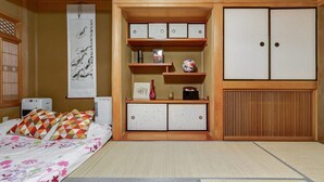 A traditional Japanese-style room with tatami flooring, a low wooden bed, a shoji screen, and a built-in wardrobe with sliding doors. - Nakayama Guesthouse (Osaka)