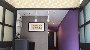 A reception area with a grey wall, a reception desk, and a sign with Japanese text. - Nakayama Guesthouse (Osaka)