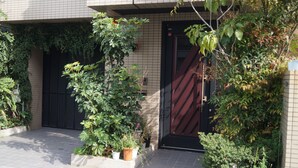A building entrance with a tiled facade, a black door, and potted plants. - Nakayama Guesthouse (Osaka)