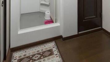 Un pasillo con cabina de ducha integrada, una puerta de madera oscura y un tapete estampado en el suelo.
