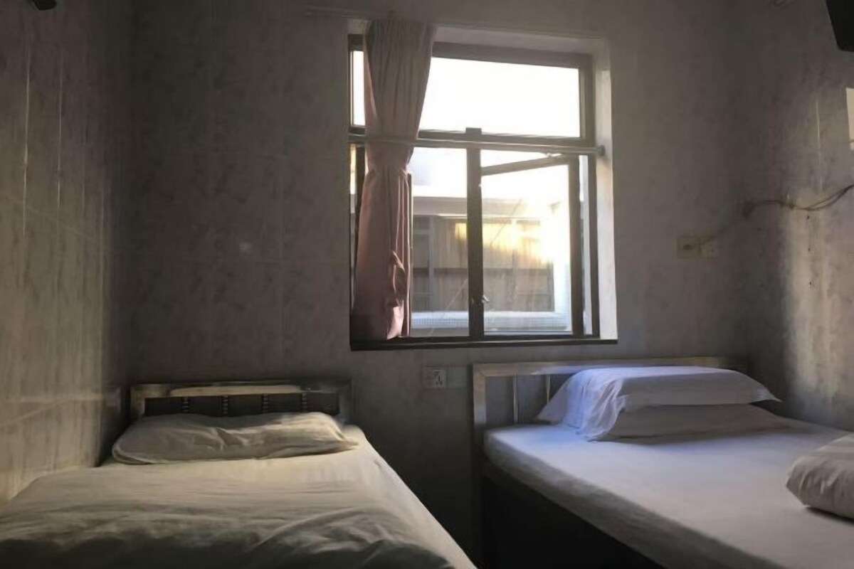 Een kamer met twee bedden, een raam met gordijnen en uitzicht op de omgeving.