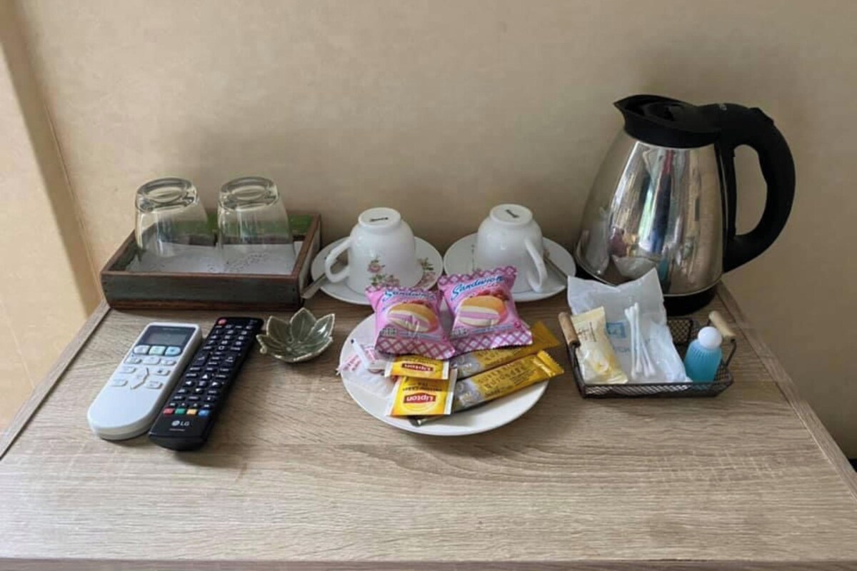 A table with a remote control, two cups, a kettle, a glass, and snacks.