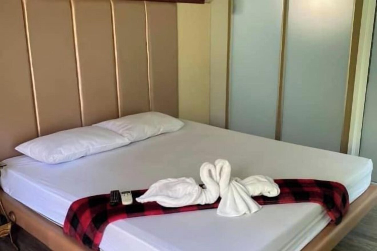 A bed with a headboard, a white pillow, and a red and black checkered blanket.
