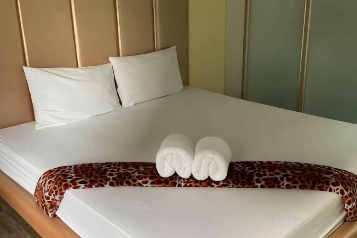 A neatly made bed with white linens, two pillows, and a brown patterned blanket.