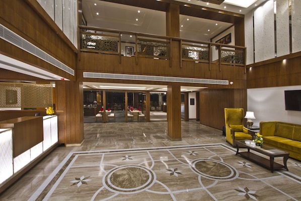 A spacious lobby with a high ceiling, wooden paneling, and a central open area with seating.