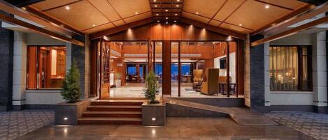 A spacious lobby with a high ceiling, wooden paneling, and a central staircase leading to upper floors.