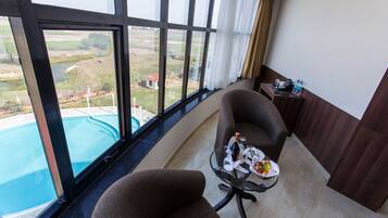 Un balcón con vista a una piscina y el paisaje, un sillón marrón, una mesita con una botella y una botella de agua en una mesita de noche.
