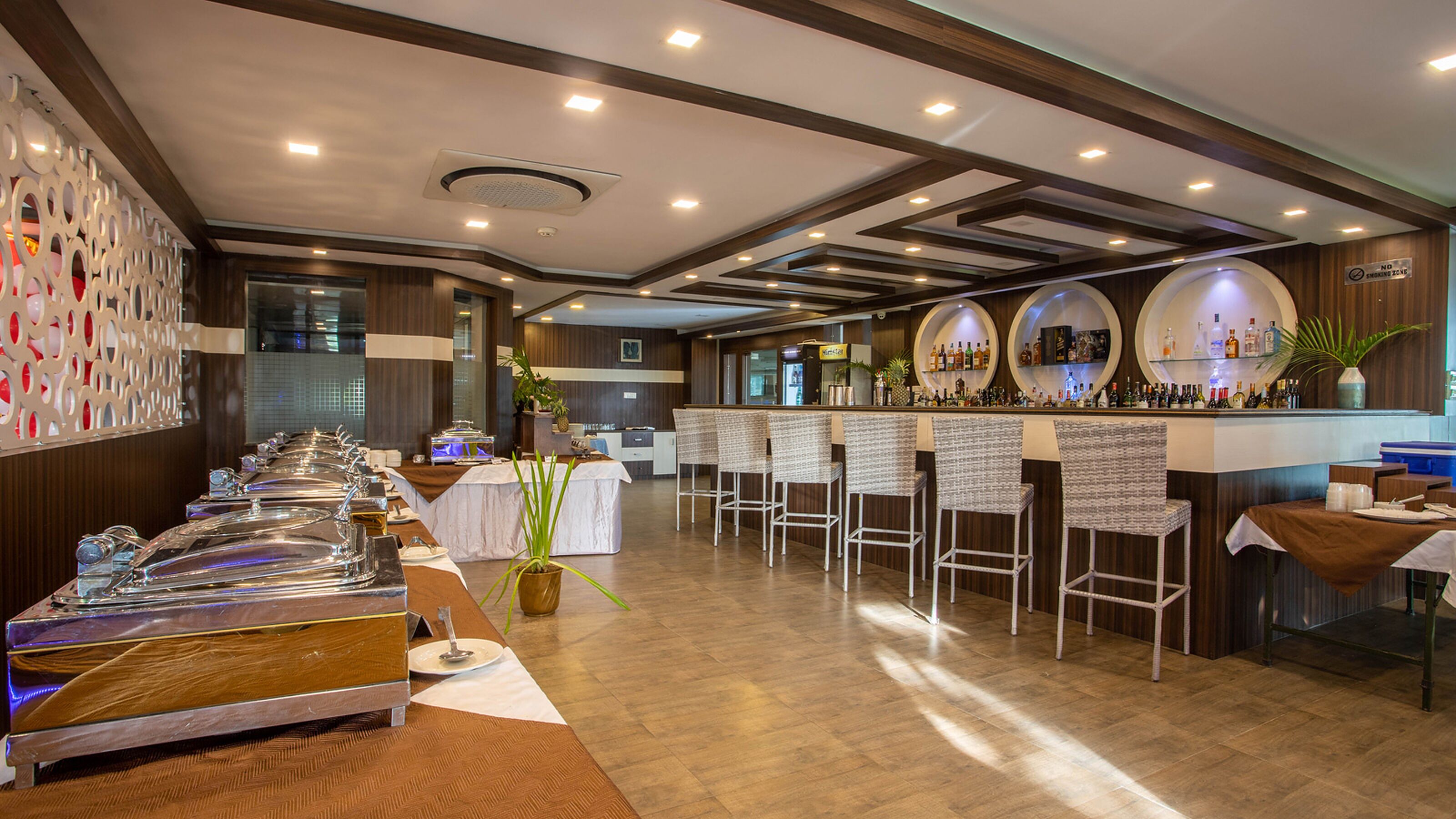 A restaurant with a long counter, multiple bar stools, and a bar area with bottles.
