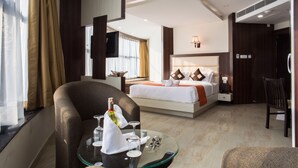 A hotel room with a bed, a glass table with a bottle and glasses, a chair, and a TV.