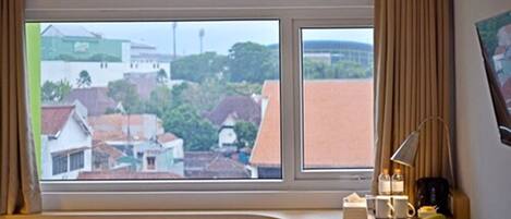 Una habitación con un amplio ventanal con vistas a una zona residencial, un escritorio con lámpara y una silla.