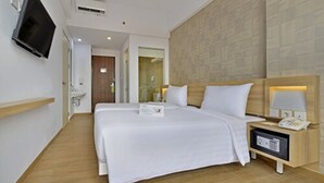 Una habitación de hotel con una cama grande, una mesita de noche con lámpara, un televisor montado en la pared y suelo de madera.