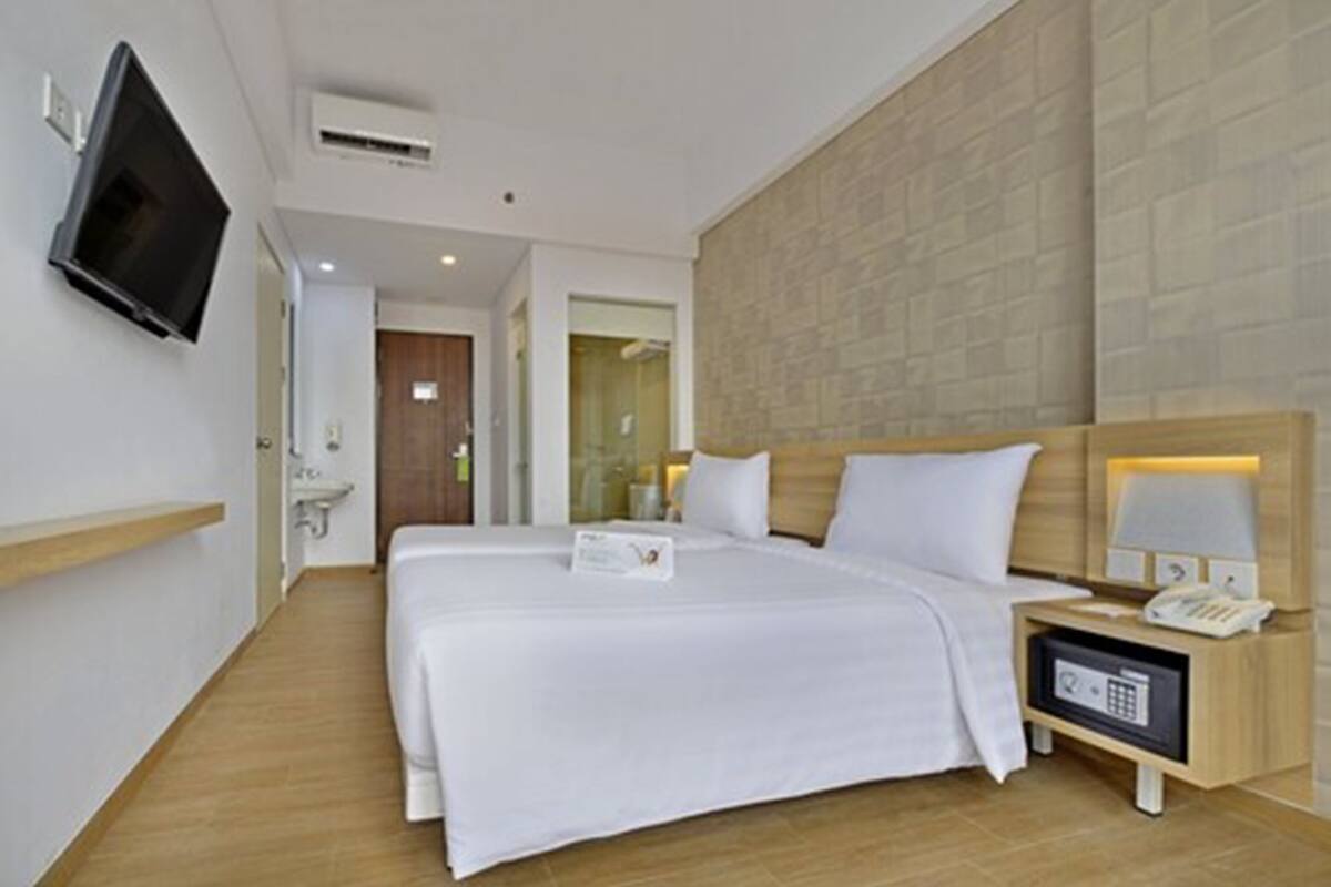 A hotel room with a large bed, a bedside table with a lamp, a TV mounted on the wall, and a wooden floor.